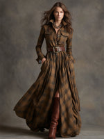 Woman wearing a long brown plaid dress with a belt and boots against a gray background
