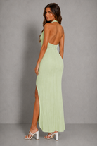 Woman wearing a light green halter neck dress with a slit on a gray background