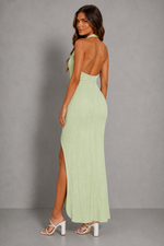 Woman wearing a light green halter neck dress with a slit on a gray background