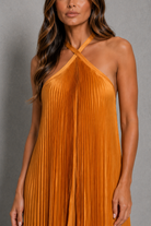 Women’s golden orange pleated halterneck maxi dress with a cross-front neckline, open back, and flowing floor-length silhouette for wedding guests and formal occasions