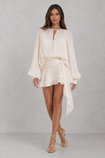 Woman wearing a white dress with long sleeves against a gray background