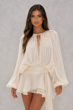 Woman wearing a beige long-sleeve dress against a gray background