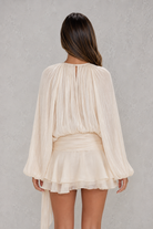 Woman wearing a beige pleated top and skirt set against a gray background