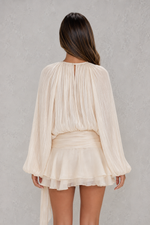 Woman wearing a beige pleated top and skirt set against a gray background