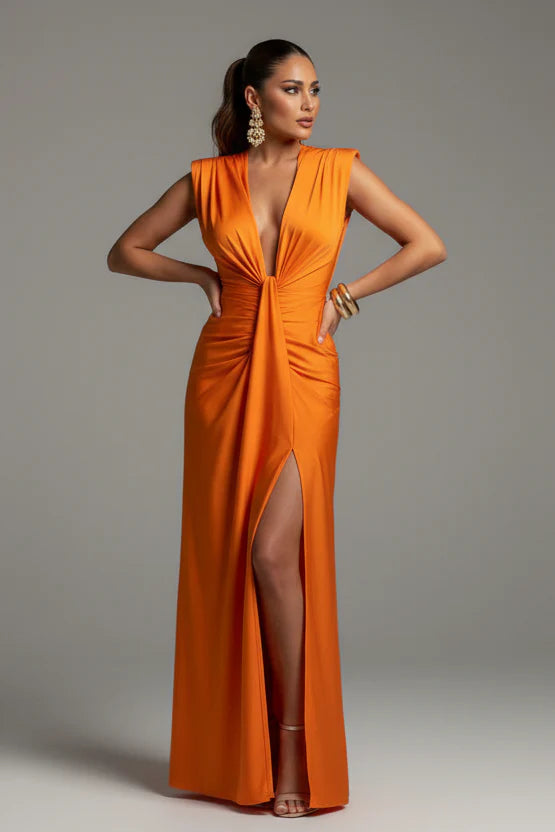 Woman wearing an orange evening gown with a deep neckline and slit on a gray background