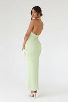 Woman wearing a light green open-back dress against a stone wall.