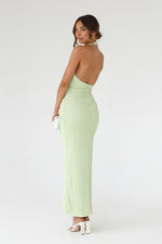 Woman wearing a light green open-back dress against a stone wall.