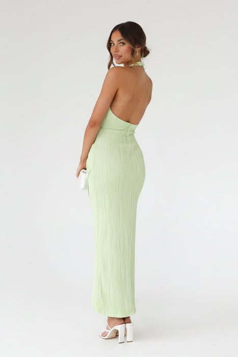 Woman wearing a light green open-back dress against a stone wall.