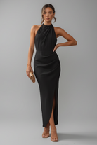 Woman in a black dress standing against a stone wall.