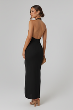 Woman in a black dress standing against a stone wall.