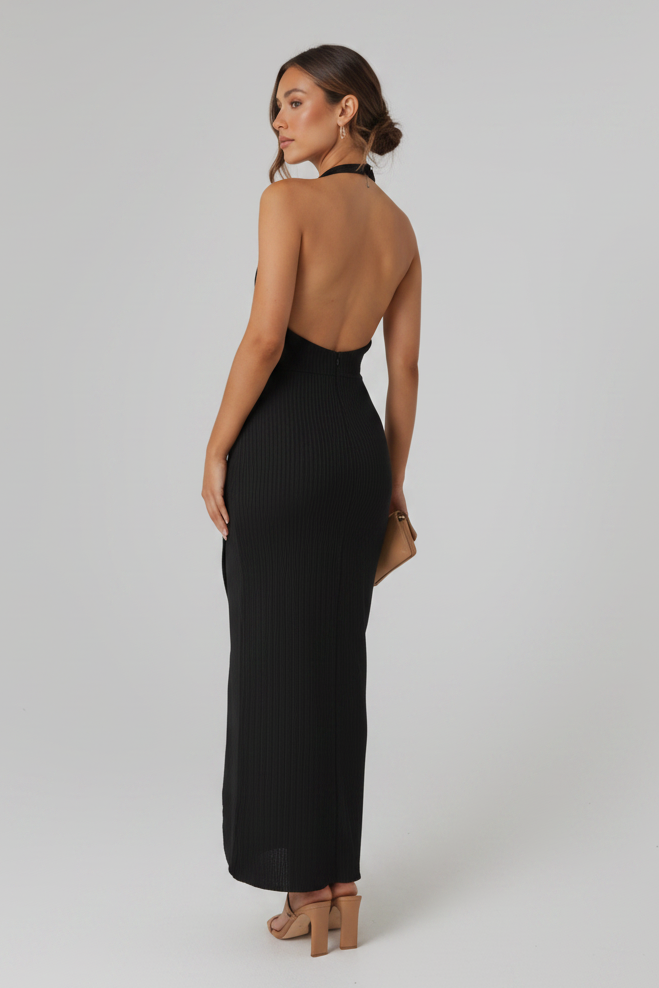 Woman in a black dress standing against a stone wall.