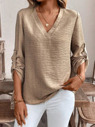 Person wearing a beige long-sleeve top and white pants in an indoor setting.