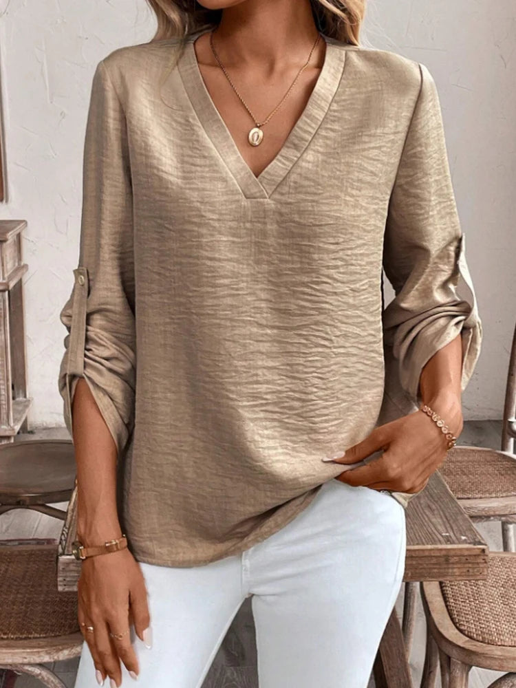 Person wearing a beige long-sleeve top and white pants in an indoor setting.