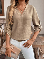 Woman wearing a beige long-sleeve top and white pants, holding a beige clutch.
