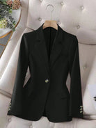 Black blazer on a hanger against a neutral background