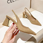 Beige high-heeled shoes held by a hand with a beige box in the background