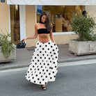 Woman in a black strapless top and white polka dot skirt walking on a street.
