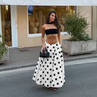 Woman in a black strapless top and white polka dot skirt standing on a street.