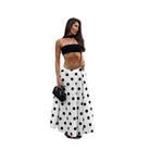 Woman wearing a black strapless top and white polka dot pants on a white background