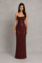 Woman wearing a strapless burgundy sequin gown against a gray background