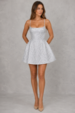 Woman wearing a white patterned dress against a gray background