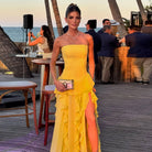 Woman in a yellow strapless dress with an orange slit standing on a wooden deck by the sea.