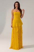 Woman wearing a yellow strapless gown with ruffled layers on a white background