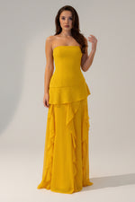 Woman wearing a yellow strapless gown with ruffled layers on a white background