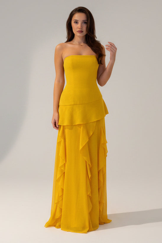 Woman wearing a yellow strapless gown with ruffled layers on a white background