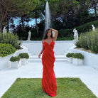 Woman in a red dress standing in a garden with a fountain and statues.