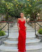 Woman in a red dress standing on stone steps with greenery and flowers in the background