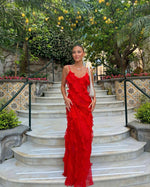 Woman in a red dress standing on stone steps with greenery and flowers in the background