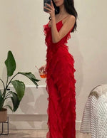 Woman in a red ruffled dress holding a drink, standing in a room with a plant and chair.