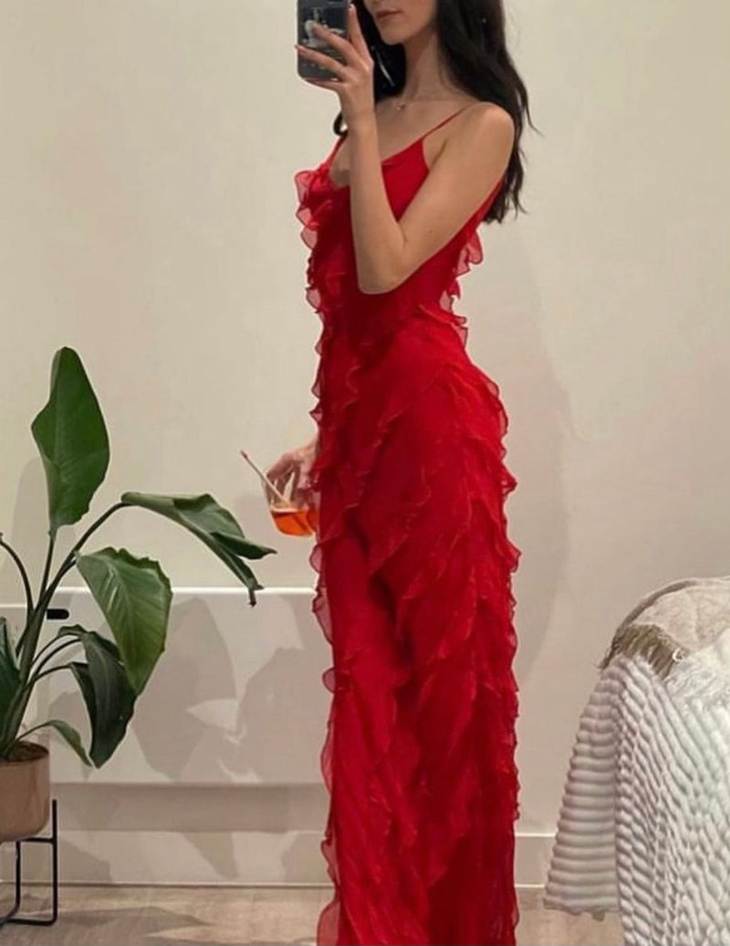 Woman in a red ruffled dress holding a drink, standing in a room with a plant and chair.