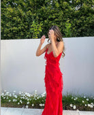Woman in a red dress standing outdoors against a white wall with greenery.