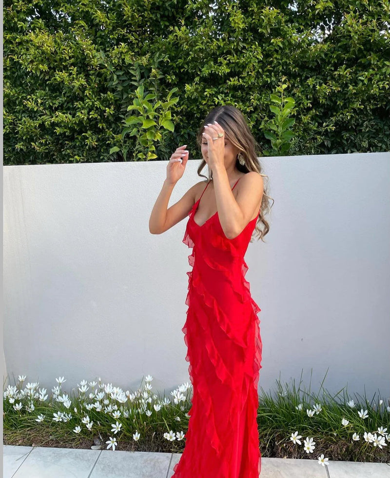 Woman in a red dress standing outdoors against a white wall with greenery.