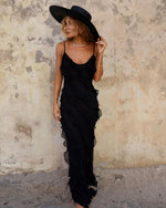 Woman wearing a black dress and hat against a textured wall.