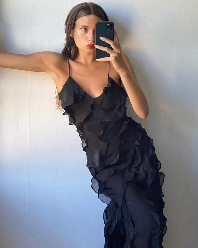 Woman taking a mirror selfie wearing a black ruffled dress against a plain background