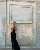 Woman in a black dress standing against an ornate stone wall.