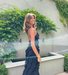 Woman in a dark blue dress standing outdoors with greenery in the background