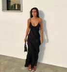 Woman wearing a black ruffled dress against a white wall.