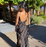 Woman in a black evening gown with a high slit standing outdoors.
