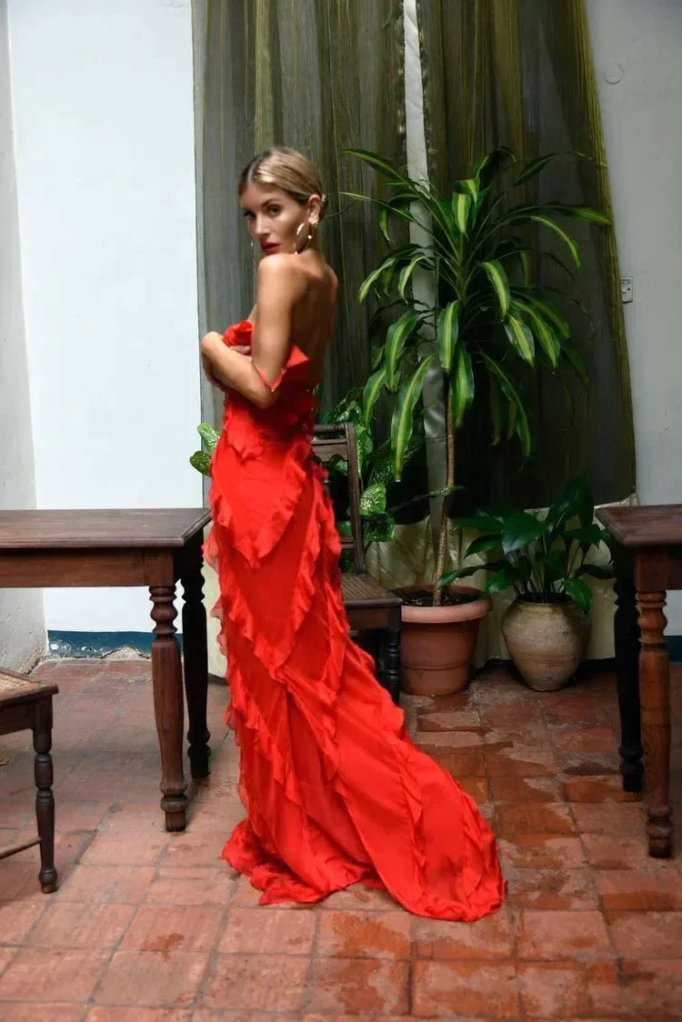 Woman in a red dress standing in a room with plants and wooden furniture.