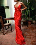 Woman wearing a red dress in an outdoor setting with plants and a table.