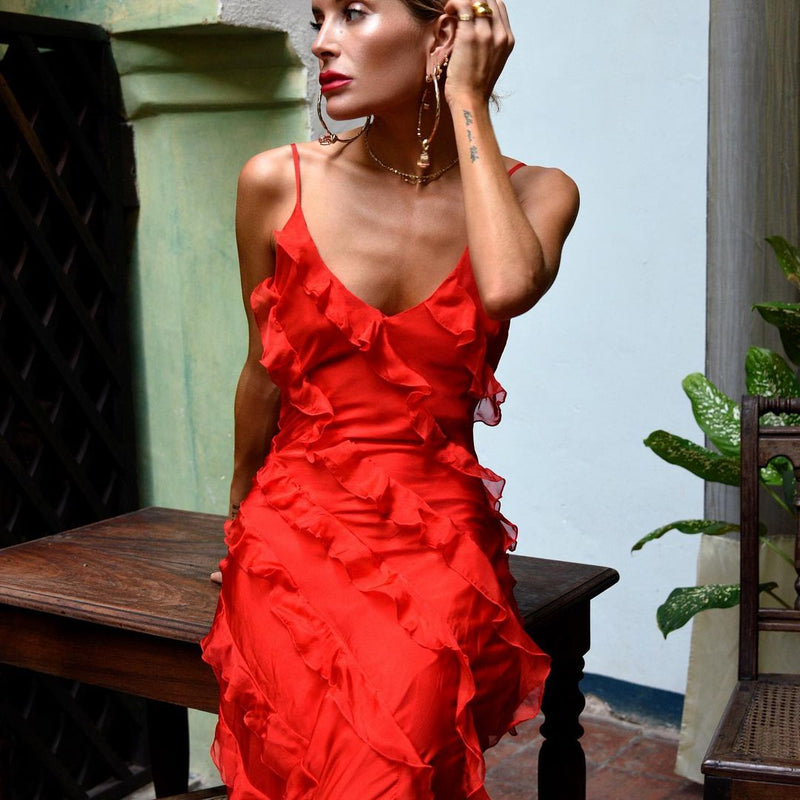 Woman in a red dress sitting on a wooden bench with a light blue wall and plant in the background.