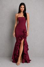 Woman wearing a burgundy strapless gown with ruffle details against a gray background