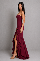 Woman wearing a burgundy one-shoulder dress with ruffles on a gray background
