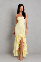 Woman wearing a light yellow strapless dress with ruffled skirt against a gray background