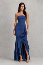 Woman wearing a strapless, ruffled navy blue gown against a gray background