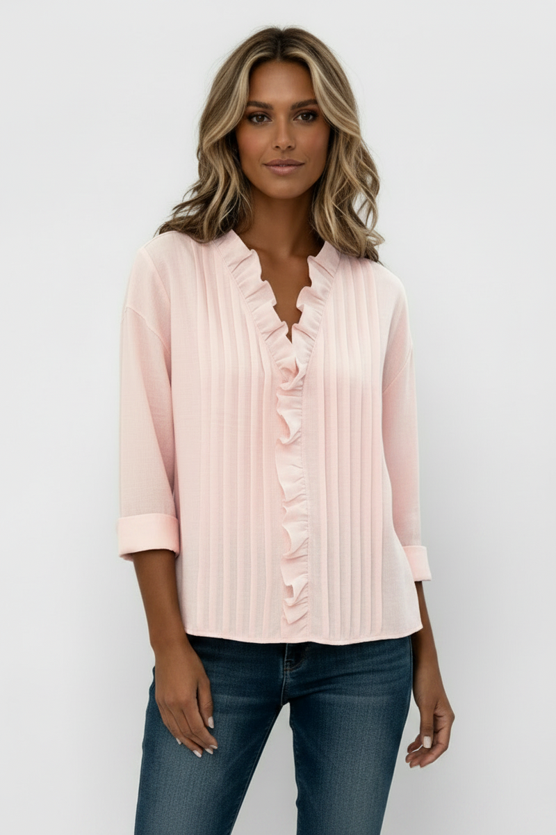 Person wearing a light pink blouse with ruffled details on a plain background